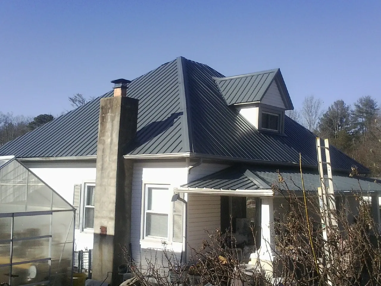 Dark blue standing seam metal roof on a white farmhouse with dormer — Slate & Tile Roof Repair by Roofing Brothers in Sparta