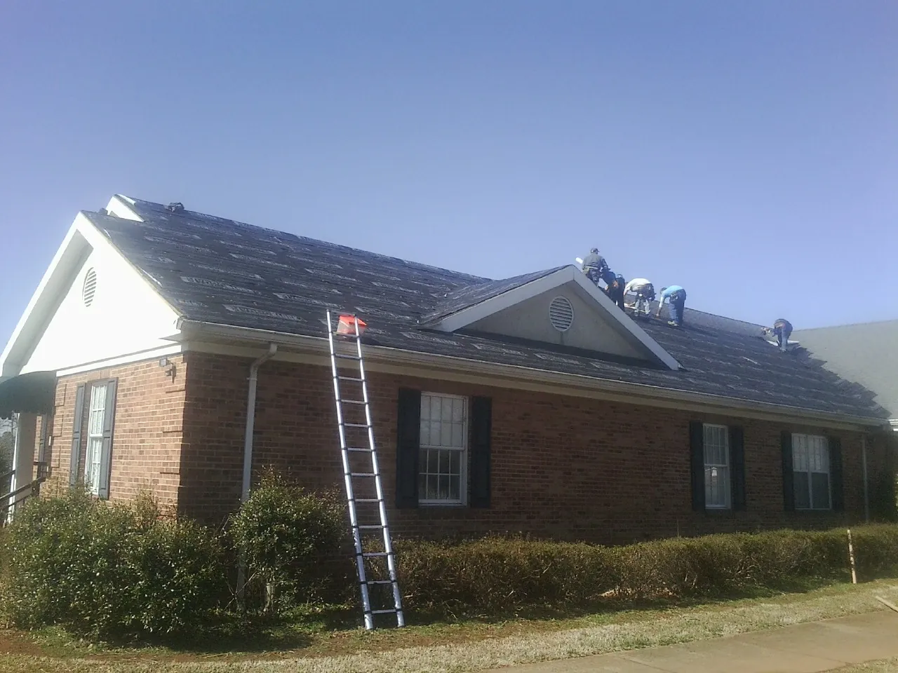 Crew tearing shingles off a brick ranch roof with a ladder set — Metal Roof Repair work by our crew in Sparta