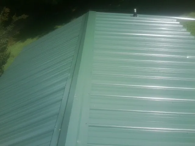 New green metal panels meeting at the ridge of a roof — Flat Roof Repair work by our crew in Sparta