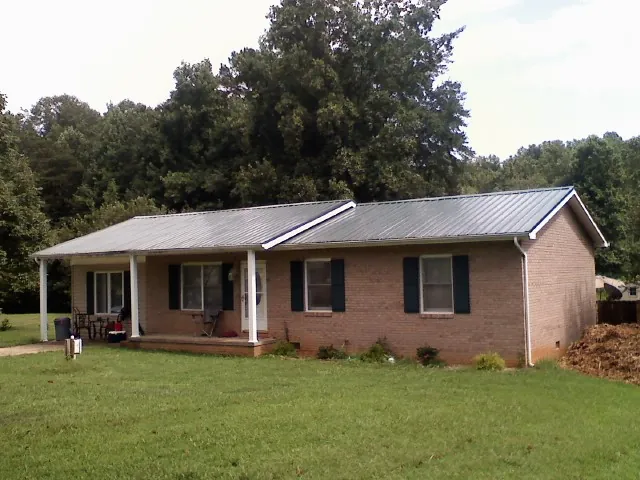 Gray metal roof on a brick ranch house with a side carport in Sparta